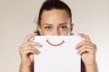 Frau hält sich Papier mit Smiley-Mund vor das Gesicht