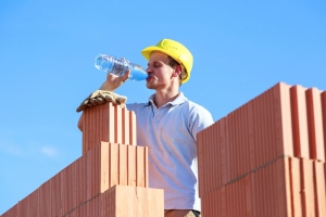 Durstiger Arbeiter auf einer Baustelle trinkt aus einer Wasserflasche