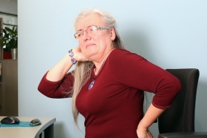 Frau mit schmerzverzerrtem Gesicht aufgrund von Nacken- und Rückenschmerzen