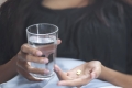 Frau hält Glas Wasser und Tabletten in den Händen