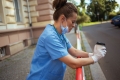 Krankenschwester steht vor Spital mit Kaffee und heruntergezogenem Mund-Nasen-Schutz