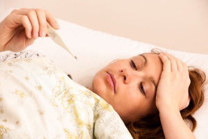Frau mit Fieberthermometer liegt krank im Bett
