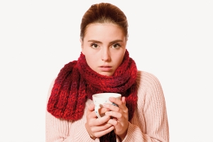 Erkältete Frau mit Schal und Teehäferl